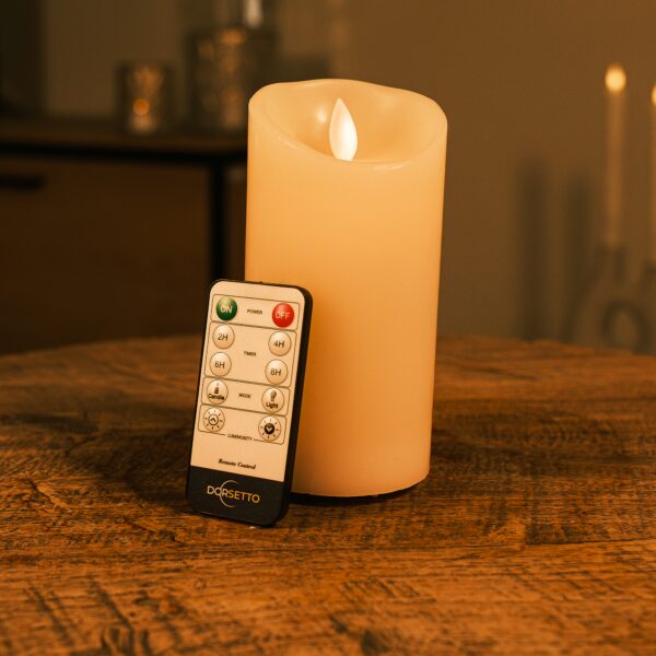 De oplaadbare LED wax kaars D 7,5 x 15 cm in warm wit staat op een houten tafel in een sfeervol verlichte kamer.