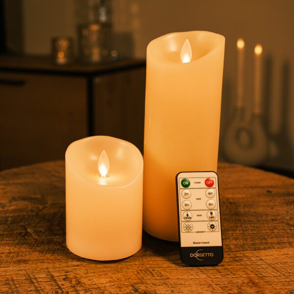 Een set van twee oplaadbare led kaarsen van Dorsetto, een hoge en een korte, staan op een houten tafel met een afstandsbediening met Dorset-label ervoor en een zacht verlichte, onscherpe achtergrond.