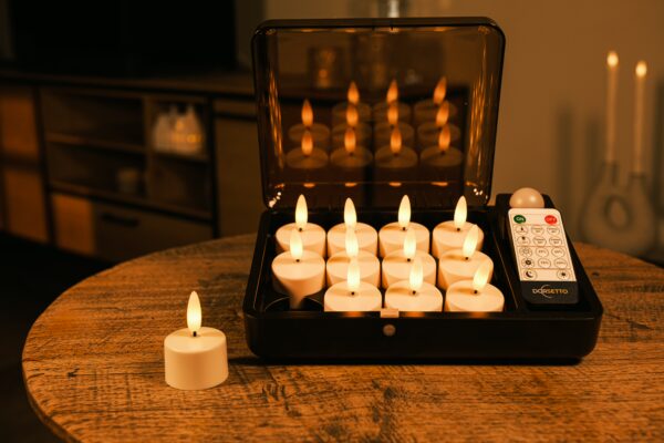 Een set van 12 oplaadbare LED waxinelichtjes 3D (tot 400 uur brandtijd) met timer en afstandsbediening, een weergegeven op een houten tafel. De warme verlichting creëert een gezellige sfeer, terwijl de afstandsbediening in de kist rust.