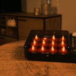 Een zwart dienblad met 12 oplaadbare rode LED-kaarsjes (175 uur, waterdicht, timerfunctie) en een afstandsbediening staat op een houten tafel in een gezellige, warm verlichte woonkamer.