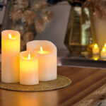 De led kaarsen set 3 kaarsen warm wit oplaadbaar DORSETTO staat op een ronde geweven mat op een houten tafel, met wazige kaarsen en vazen op de achtergrond voor een warme, gezellige sfeer.