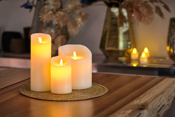 De led kaarsen set 3 kaarsen warm wit oplaadbaar DORSETTO staat op een ronde geweven mat op een houten tafel, met wazige kaarsen en vazen op de achtergrond voor een warme, gezellige sfeer.