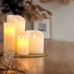 De LED wax kaarsen set 4 kaarsen warm wit oplaadbaar DORSETTO gloeit warm op een houten tafel, uitgestald op een gouden dienblad met decoratieve bladeren, en creëert een gezellige en feestelijke sfeer.