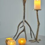 Twee metalen talonvormige kaarsenhouders houden pilaarkaarsen vast, terwijl drie Oplaadbare LED waxinelichtjes met bewegende vlam D 7,5 X 10 CM - warm wit votiefkaarsen gloeien op een grijs oppervlak en een gezellige en uitnodigende sfeer creëren.