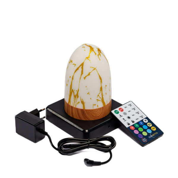 De Tafellamp DORSETTO oplaadbaar 105 uur, een ovale waterdichte lamp in marmer goud met afstandsbediening, staat op een zwarte plaat naast een oplader en een meerkleurige afstandsbediening.