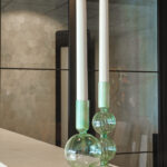 Twee LED dinerkaars 270mm oplaadbaar (130 uur warm wit, 6 stuks met afstandsbediening) in groene glazen houders gloeien warm op een licht aanrechtblad en versterken het moderne interieur met glazen panelen en betegelde wanden.