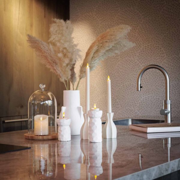Een modern marmeren aanrecht toont witte vazen met pampagras, een glazen cloche boven een kaars, boeken en LED waxinelichtjes 3D (175u brandtijd, oplaadbaar, afstandsbediening, timerfunctie), 12-delige set bij een roestvrijstalen kraan.