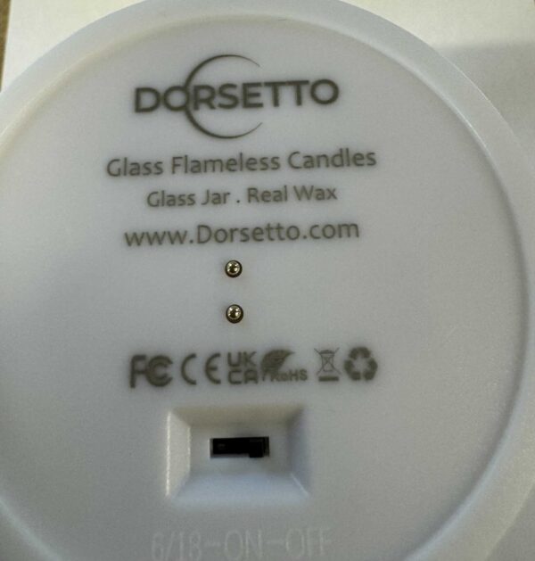 Close-up van de onderkant van een DORSETTO led kaarsen set - oplaadbaar 105 uur, 3D vlam, met afstandsbediening, met de merknaam, productinformatie, certificeringen, website en aan-uitschakelaar.