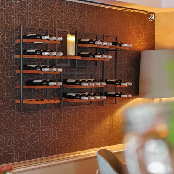 Een modern wijnrek aan de muur toont verschillende wijnflessen en een grote kaars boven een eettafel, aangevuld met de DORSETTO LED kleine was kaarsen set 2 kaarsen voor extra sfeer tegen een bruine muur met patroon.