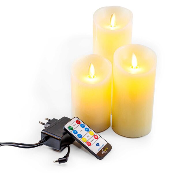 Drie Oplaadbare LED wax kaarsen van 3 stuks DORSETTO in verschillende hoogtes staan bij elkaar en stralen een warmgeel licht uit. Een afstandsbediening en stroomadapter zijn vooraan geplaatst.
