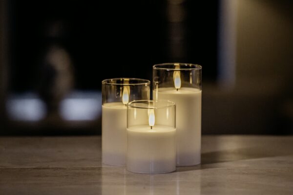 De DORSETTO led kaarsen set - oplaadbaar 105 uur met 3D vlam en afstandsbediening brandt sfeervol dichtbij elkaar in glazen houders op een egale ondergrond, tegen een zacht vervaagde donkere achtergrond.