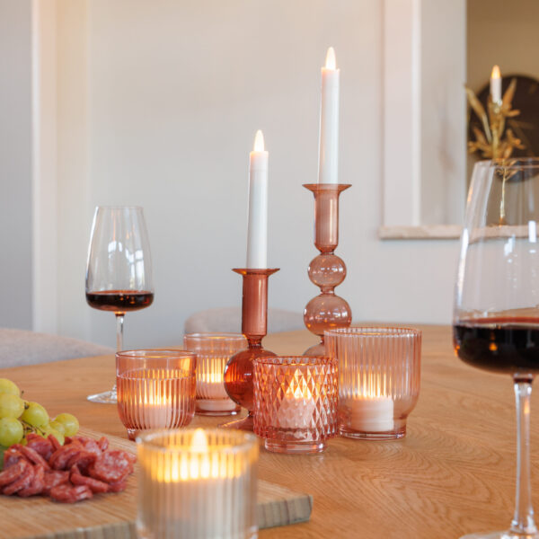 Een houten gedekte tafel met warmwitte oplaadbare LED-waxine/theelichtjes (12 stuks, 175 uur brandtijd, waterdicht, met afstandsbediening) in roze glazen houders, rode wijnglazen en een schotel met druiven en gesneden vlees creëert een gezellige eetvibe.