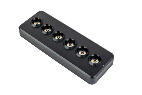 De Oplaadstation zwart magnetisch DORSETTO voor 6 dinerkaarsen is een slank zwart oplaaddock met zes ronde sleuven, ideaal voor het opladen van maximaal zes dinerkaarsen of andere kleine apparaten, afgebeeld op een witte achtergrond.