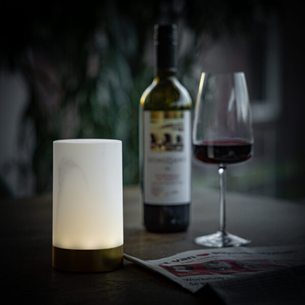 De set van 2 cilindervormige led Tafellamp DORSETTO oplaadbaar 105 uur in marmer met grijs houtlook, waterdicht en met afstandsbediening, zorgt voor een gezellige sfeer op tafel naast een glas rode wijn en een krant.