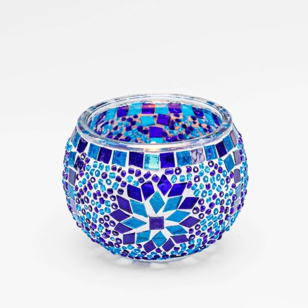 Theelichthouder 9 CM Dorsetto blauw: een ronde glazen kandelaar, versierd met blauwe, paarse en witte geometrische mozaïektegeltjes en een stervormig ontwerp. Gefotografeerd tegen een effen witte achtergrond.
