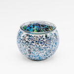 Een 9 cm ronde glazen Waxinelichthouder Dorsetto mozaïek multicolor, met kleine, onregelmatige blauwe en zilveren mozaïeksteentjes, afgebeeld op een effen witte achtergrond.