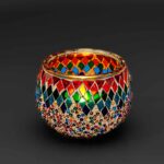 Theelichthouder gekleurde spikkels 9 CM DORSETTO: een ronde glazen kandelaar met levendige rode, blauwe, groene en gouden mozaïekdiamanten op een opvallende zwarte achtergrond.