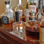 Verschillende flessen whisky en andere sterke dranken staan op een spiegelschaal naast een LED-Waxine/theelichtjes waterdicht oplaadbaar brandtijd 175 uur warm wit (12 stuks) met afstandsbediening glazen kandelaar.