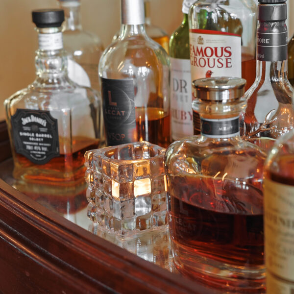 Verschillende flessen whisky en andere sterke dranken staan op een spiegelschaal naast een LED-Waxine/theelichtjes waterdicht oplaadbaar brandtijd 175 uur warm wit (12 stuks) met afstandsbediening glazen kandelaar.