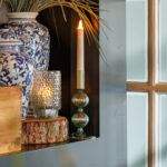 Een witte kaars en blauw-witte vaas met gedroogd gras inspireren met LED waxine lichtjes oplaadbaar met afstandsbediening waterdicht brandtijd 175 uur op een houten plank bij het matte raam voor een gezellige, veilige gloed.