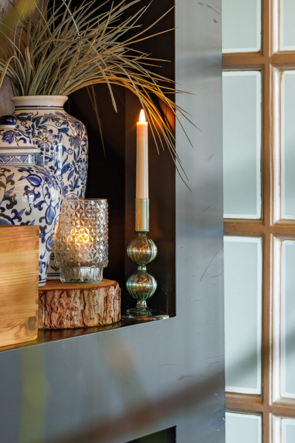 Een witte kaars en blauw-witte vaas met gedroogd gras inspireren met LED waxine lichtjes oplaadbaar met afstandsbediening waterdicht brandtijd 175 uur op een houten plank bij het matte raam voor een gezellige, veilige gloed.