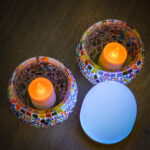 Twee mozaïek glazen kandelaars met oranje LED kaarsen staan op een houten oppervlak naast een Oplaadbaar LED waxine/theelichtje 175 uur waterproof warm wit, onderdeel van een 6-delige set met afstandsbediening.
