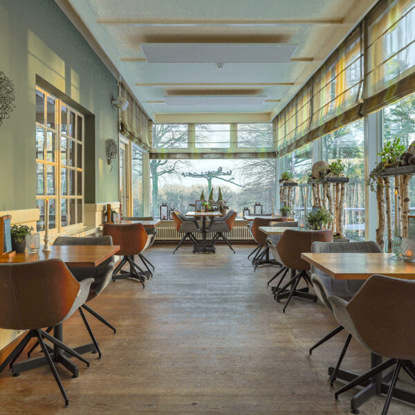 Een licht, modern restaurant met bruine stoelen en houten tafels die netjes zijn gerangschikt. Grote ramen bieden natuurlijk licht en uitzicht op bomen. LED waxine lichtjes oplaadbaar met afstandsbediening waterdicht brandtijd 175 uur versterken de gezellige sfeer.
