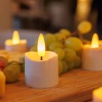 De 3D oplaadbare LED-thee/waxinelichtjes (12 stuks, 175 uur, met afstandsbediening en timerfunctie) zorgen voor een warme, gezellige sfeer op een houten oppervlak naast een tros groene druiven.