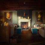 Een gezellige lounge met sofa's, een brandende open haard, Oplaadbare LED wax kaarsjes D 7,5 X 15 CM - warm wit kaarsen, en twee grote portretten. Een hertenkop boven de schouw en blauwe poefs bij het vuur maken de ruimte, badend in warme verlichting, compleet.