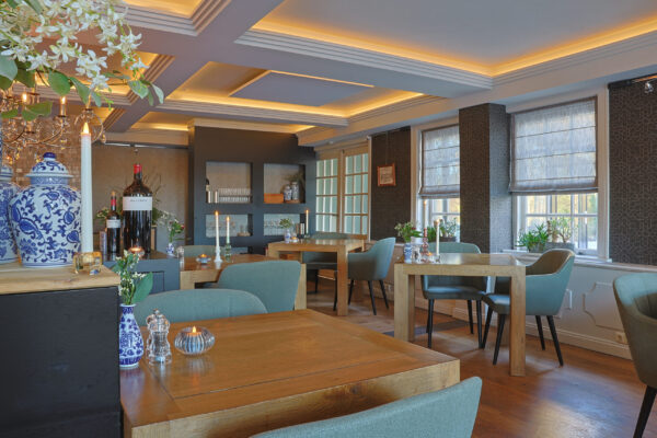 Een stijlvol restaurant met houten tafels, groene stoelen, grote ramen met vouwgordijnen, elegante verlichting en accenten zoals een blauw-witte vaas en oplaadbare LED waxine/theelichtjes 175 uur waterdicht warm wit (6 stuks) met afstandsbediening.