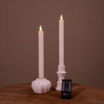 De Dinerkaarsen LED set van 2 (400 uur oplaadbaar, wit) zit in keramische houders - de ene rond en geribbeld, de andere klassiek - op hout, met een afstandsbediening ervoor.