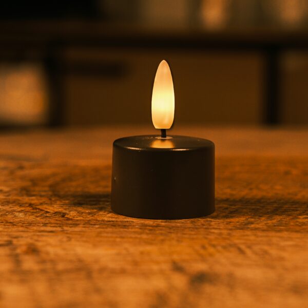 Een kleine LED-kaars op batterijen met een warm, flikkerend licht staat op een houten oppervlak en creëert een gezellige sfeer. De achtergrond is zacht vervaagd.