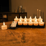 Twaalf Oplaadbare waxinelichtjes met realistische 3D vlammen, 140 branduren en afstandsbediening staan op een houten tafel en geven een zachte, gezellige gloed op de achtergrond.