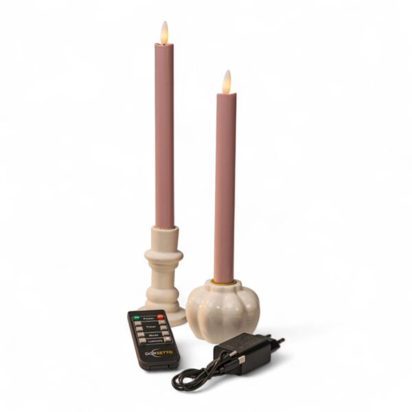 Twee roze kaarsen op batterijen in witte houders, een afstandsbediening en een zwarte voedingsadapter staan op een witte achtergrond. De kaarsen hebben vlamvormige uiteinden die echte vlammen simuleren.